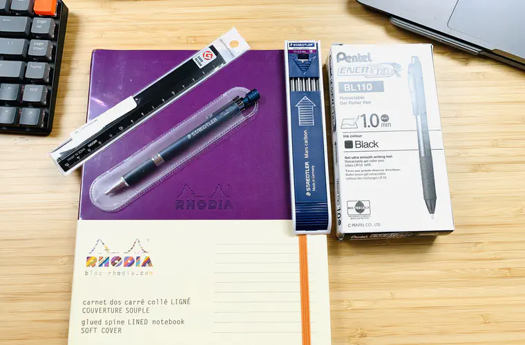A purple soft cover Rhodia notebook, Midori 15 cm aluminium rule, Staedtler Night Blue 2 mm lead holder, 2 mm Staedtler Mars carbon leads and box of Pentel 1 mm EnerGel X pens.